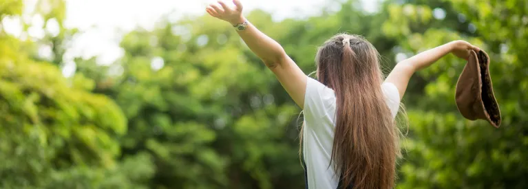 Dziewczynka z podniesionymi rękoma na tle drzew