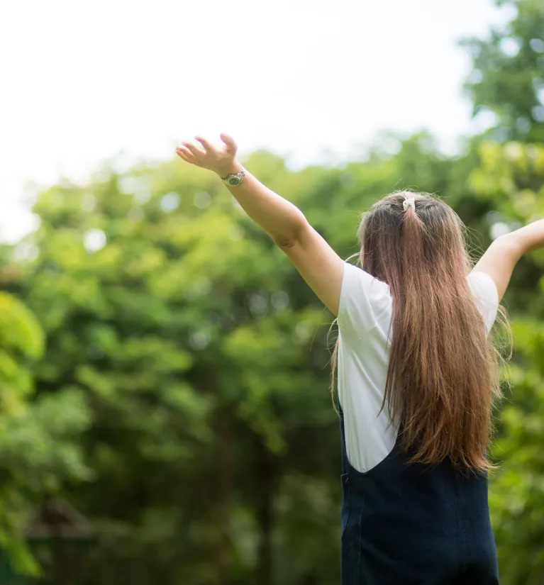 Dziewczynka z podniesionymi rękoma na tle drzew